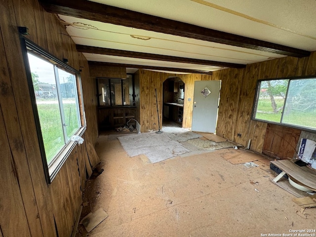 unfurnished living room featuring wooden walls and beam ceiling