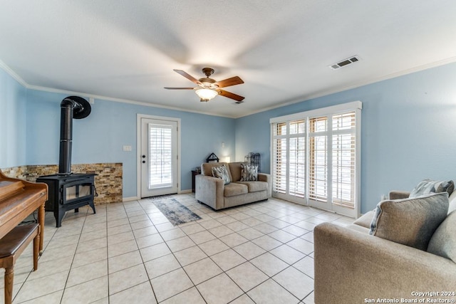 living room with ceiling fan, light tile patterned flooring, a wood stove, and crown molding