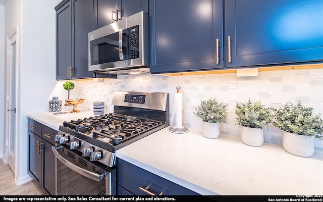 kitchen with blue cabinets, light hardwood / wood-style flooring, backsplash, and appliances with stainless steel finishes