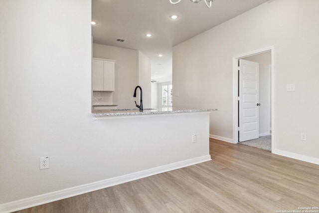 kitchen with white cabinets, sink, light hardwood / wood-style floors, light stone counters, and kitchen peninsula