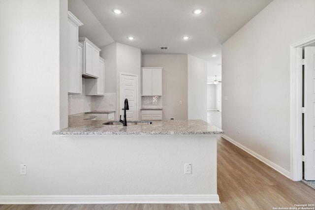 kitchen with white cabinets, sink, decorative backsplash, light stone counters, and kitchen peninsula