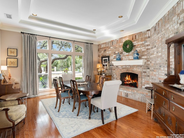 dining room with a raised ceiling, a fireplace, ornamental molding, and light hardwood / wood-style flooring