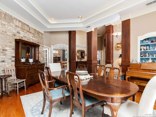 dining room featuring dark wood-type flooring, a tray ceiling, ornamental molding, and ornate columns