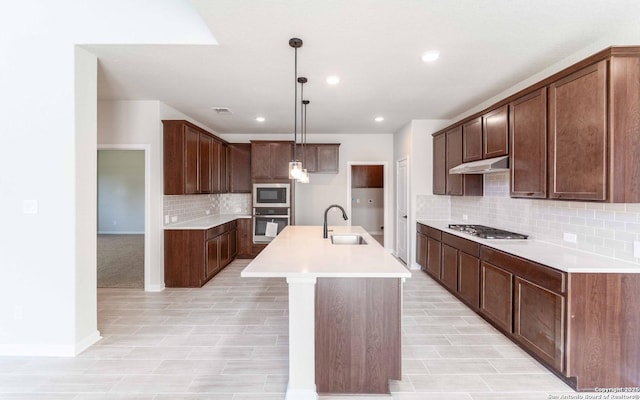 kitchen with sink, hanging light fixtures, decorative backsplash, a center island with sink, and appliances with stainless steel finishes