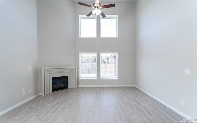 unfurnished living room with ceiling fan, light hardwood / wood-style floors, and a high ceiling