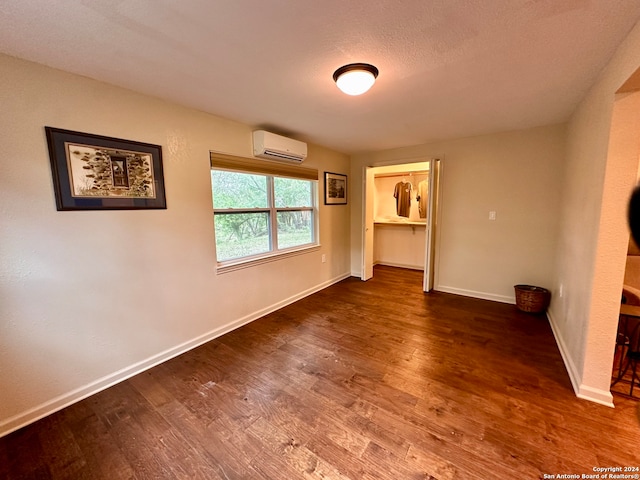 unfurnished bedroom with dark hardwood / wood-style floors, a closet, a walk in closet, and an AC wall unit