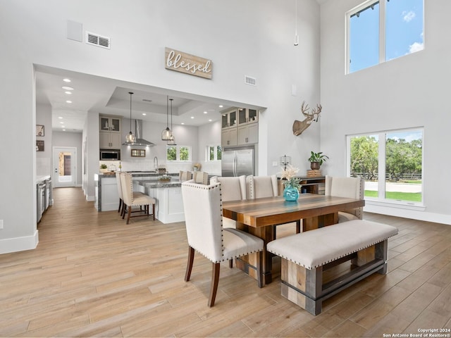 dining space featuring a high ceiling, a raised ceiling, light hardwood / wood-style flooring, and sink