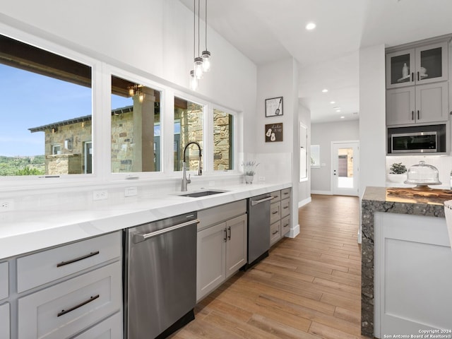 kitchen with appliances with stainless steel finishes, a healthy amount of sunlight, sink, and light hardwood / wood-style flooring