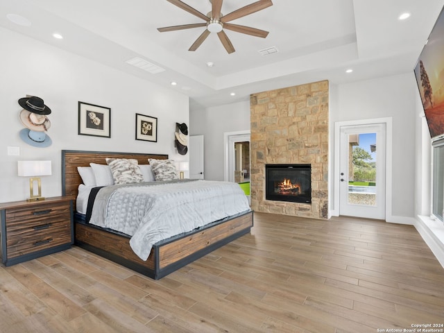 bedroom with ceiling fan, a fireplace, wood-type flooring, a raised ceiling, and access to outside