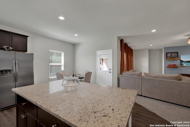 kitchen with light stone countertops, stainless steel refrigerator with ice dispenser, dark hardwood / wood-style flooring, dark brown cabinets, and a kitchen island