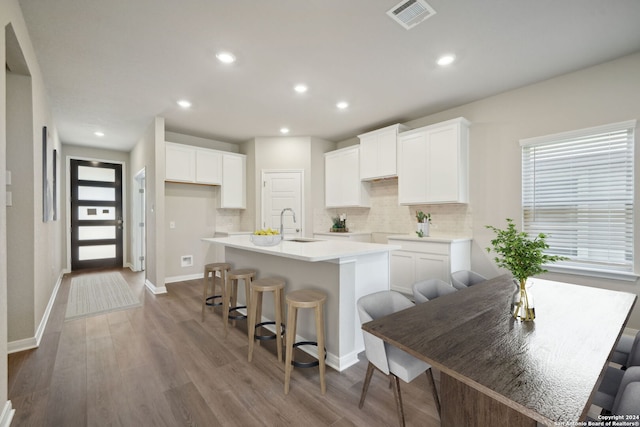 kitchen with white cabinets, dark hardwood / wood-style flooring, an island with sink, and tasteful backsplash