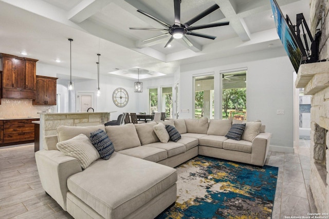 living room featuring beamed ceiling, ceiling fan with notable chandelier, a fireplace, and coffered ceiling