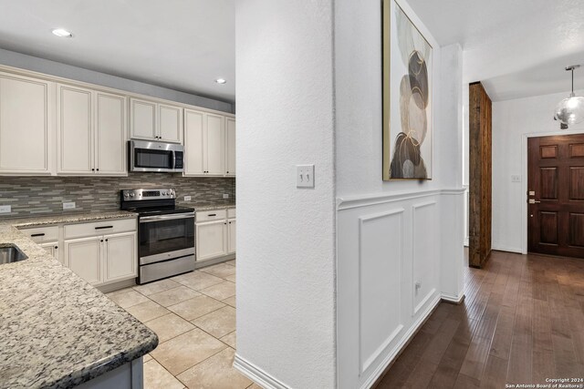 kitchen featuring light tile flooring, tasteful backsplash, light stone countertops, appliances with stainless steel finishes, and pendant lighting