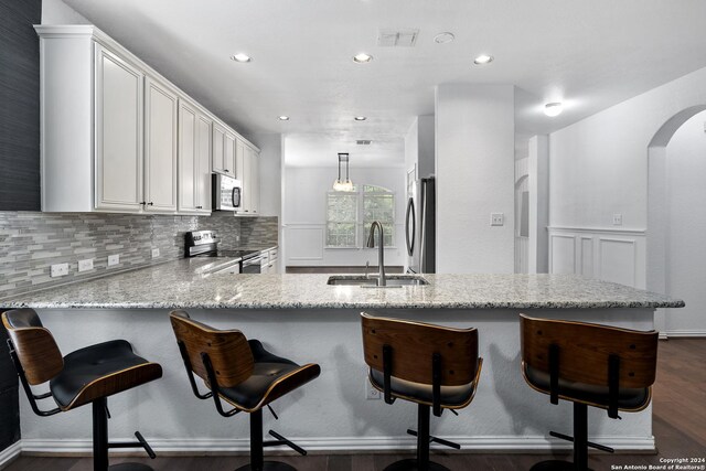 kitchen with dark wood-type flooring, stainless steel appliances, kitchen peninsula, a breakfast bar, and sink