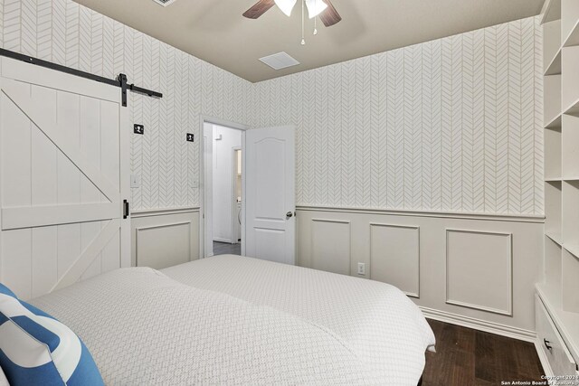 bedroom featuring a barn door, ceiling fan, and dark hardwood / wood-style flooring