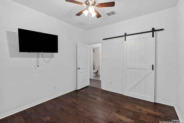 unfurnished bedroom with a barn door, ceiling fan, connected bathroom, and dark wood-type flooring