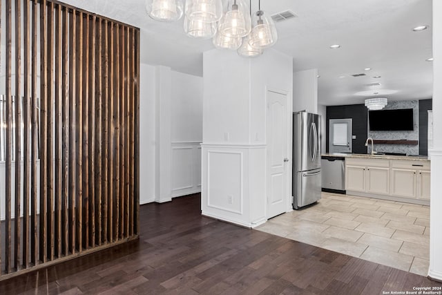 kitchen featuring stainless steel appliances, light hardwood / wood-style flooring, decorative light fixtures, sink, and white cabinets