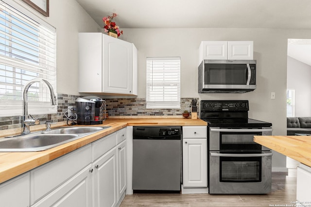 kitchen with sink, a healthy amount of sunlight, stainless steel appliances, wood counters, and white cabinets