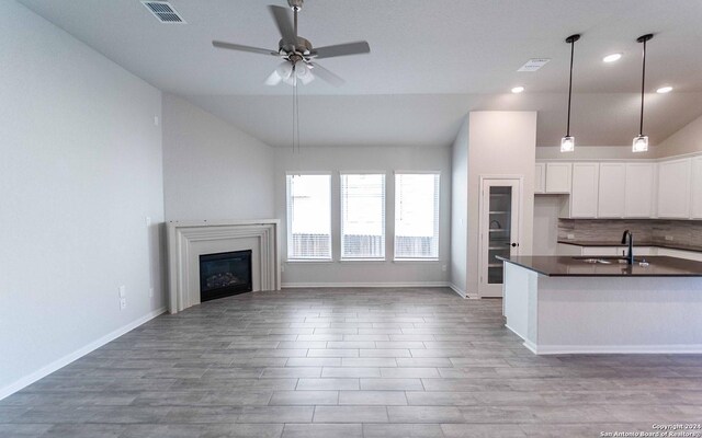 kitchen featuring lofted ceiling, sink, backsplash, white cabinets, and decorative light fixtures