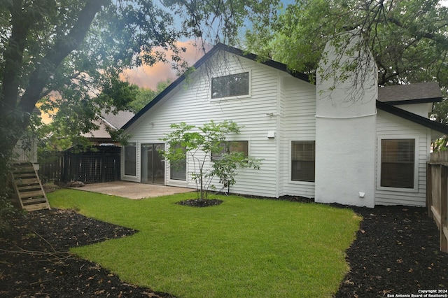 back house at dusk featuring a yard and a patio