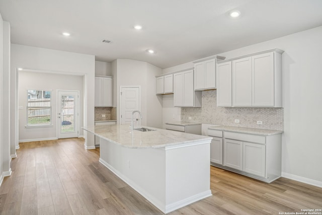 kitchen featuring an island with sink, light stone countertops, light hardwood / wood-style floors, and sink