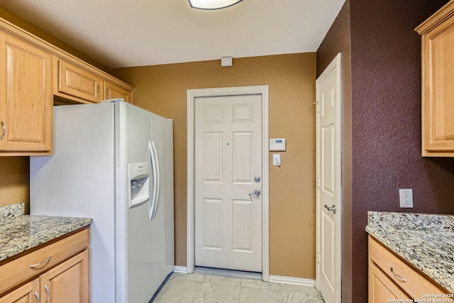 kitchen with light stone counters, light brown cabinetry, and white fridge with ice dispenser