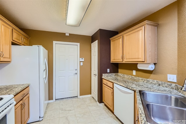 kitchen with light stone counters, white appliances, light brown cabinetry, and sink