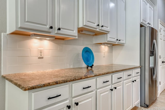 kitchen with white cabinetry, decorative backsplash, stainless steel fridge, and stone countertops