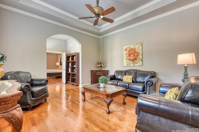 living room featuring ceiling fan, ornamental molding, light hardwood / wood-style flooring, and a tray ceiling