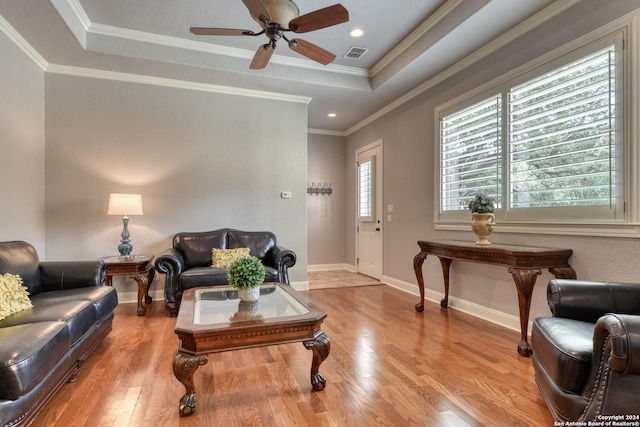 living room featuring a raised ceiling, ceiling fan, light hardwood / wood-style flooring, and ornamental molding