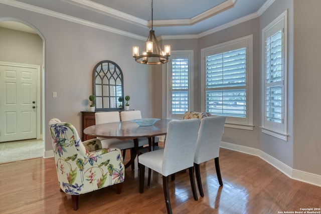 dining room featuring hardwood / wood-style floors, an inviting chandelier, a raised ceiling, and crown molding