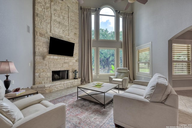 tiled living room with plenty of natural light, ceiling fan, a towering ceiling, and a fireplace