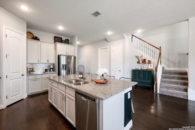 kitchen with white cabinetry, sink, light stone countertops, stainless steel appliances, and a kitchen island with sink