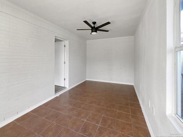 tiled spare room featuring ceiling fan and brick wall