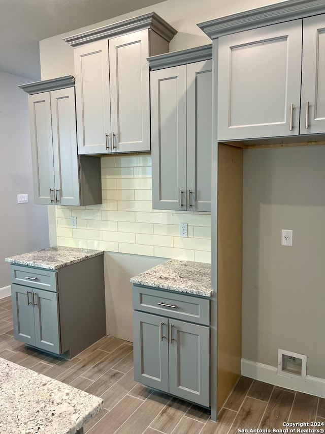 kitchen with backsplash, wood-type flooring, and light stone countertops