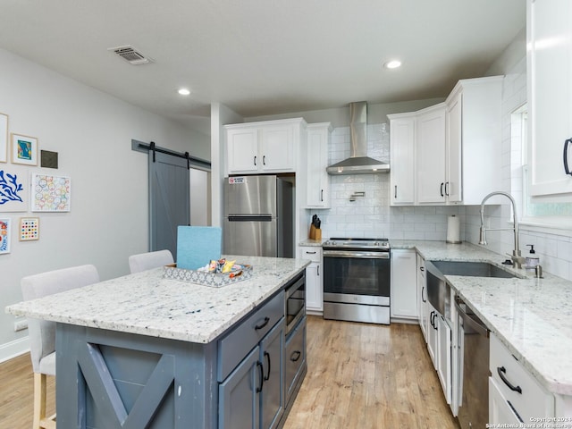 kitchen with a barn door, white cabinetry, appliances with stainless steel finishes, and wall chimney exhaust hood