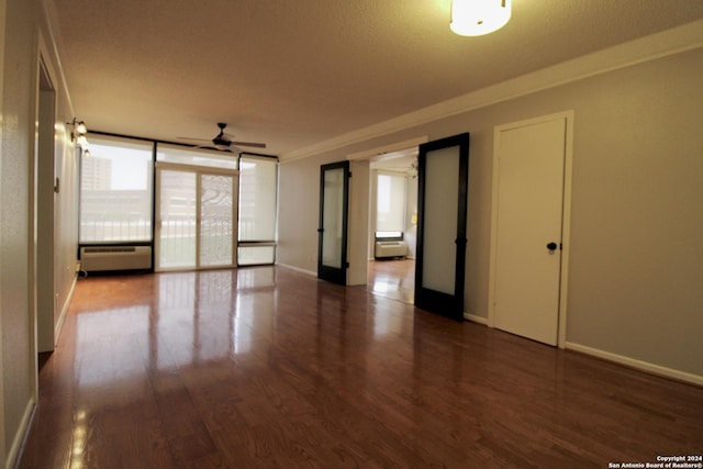 empty room with a wall of windows, ceiling fan, a baseboard heating unit, dark hardwood / wood-style floors, and ornamental molding