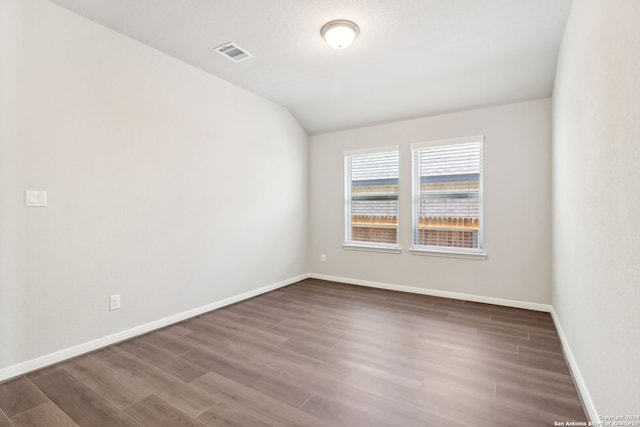 unfurnished room featuring baseboards, visible vents, vaulted ceiling, and wood finished floors