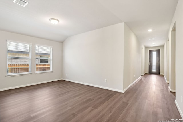 empty room featuring lofted ceiling, dark wood-type flooring, visible vents, and baseboards