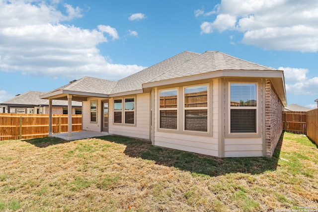 back of property with a shingled roof, a patio area, a fenced backyard, and a lawn