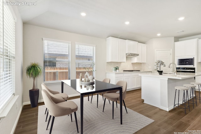 kitchen with tasteful backsplash, light countertops, a kitchen island with sink, white cabinetry, and black microwave