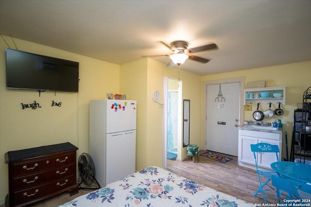 bedroom featuring ceiling fan, white fridge, ensuite bathroom, and light wood-type flooring