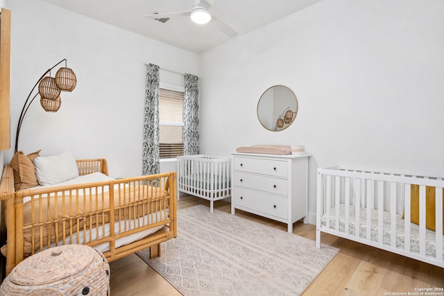 bedroom featuring ceiling fan, light hardwood / wood-style floors, and a crib