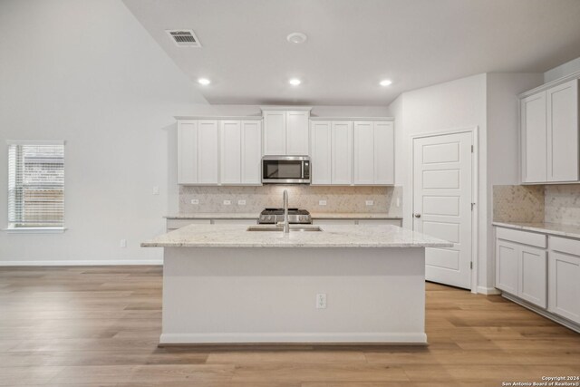 kitchen with a center island with sink, light wood-type flooring, light stone counters, sink, and white cabinetry