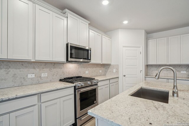 kitchen featuring stainless steel appliances, light stone countertops, sink, white cabinetry, and backsplash