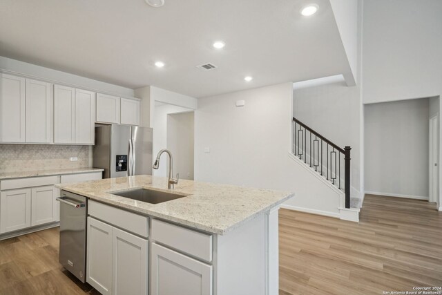 kitchen with sink, white cabinetry, light stone counters, and stainless steel refrigerator with ice dispenser