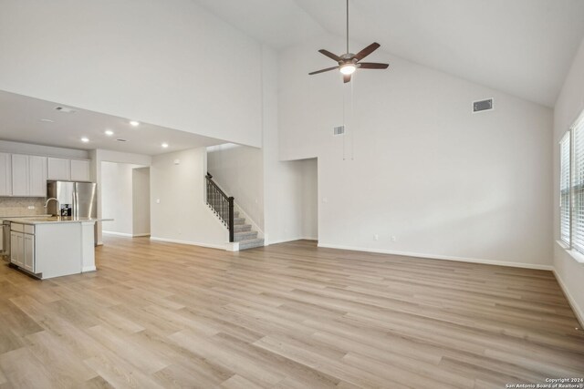 unfurnished living room with high vaulted ceiling, ceiling fan, and light hardwood / wood-style flooring