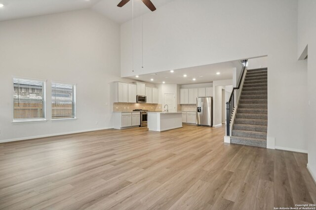 unfurnished living room with sink, high vaulted ceiling, ceiling fan, and light hardwood / wood-style flooring