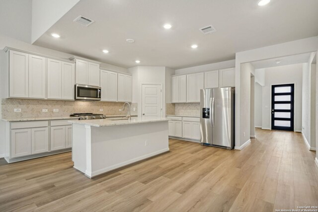 kitchen featuring light stone counters, light wood-type flooring, a kitchen island with sink, white cabinetry, and appliances with stainless steel finishes