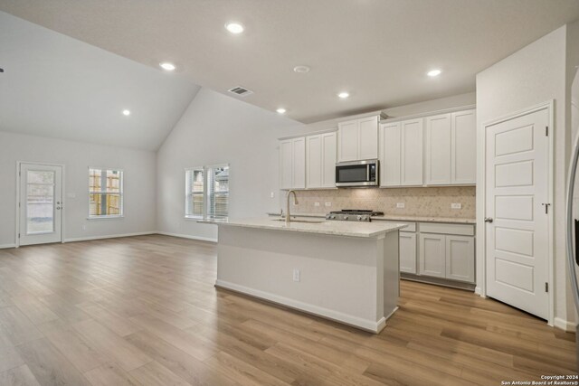 kitchen featuring sink, white cabinetry, vaulted ceiling, light wood-type flooring, and a center island with sink